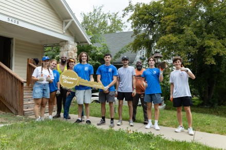 Students pose outside a renovated home with a large key that says Welcome Home