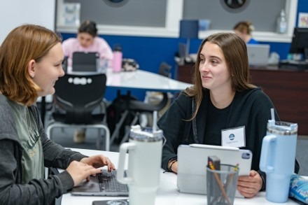 Two girls look at each other while on their laptops in the Learning Center
