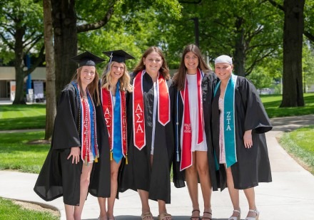 Group of graduates wearing sorority stoles with their caps and gowns